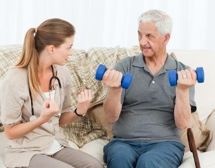 Older man exercising at home with the help of a caregiver